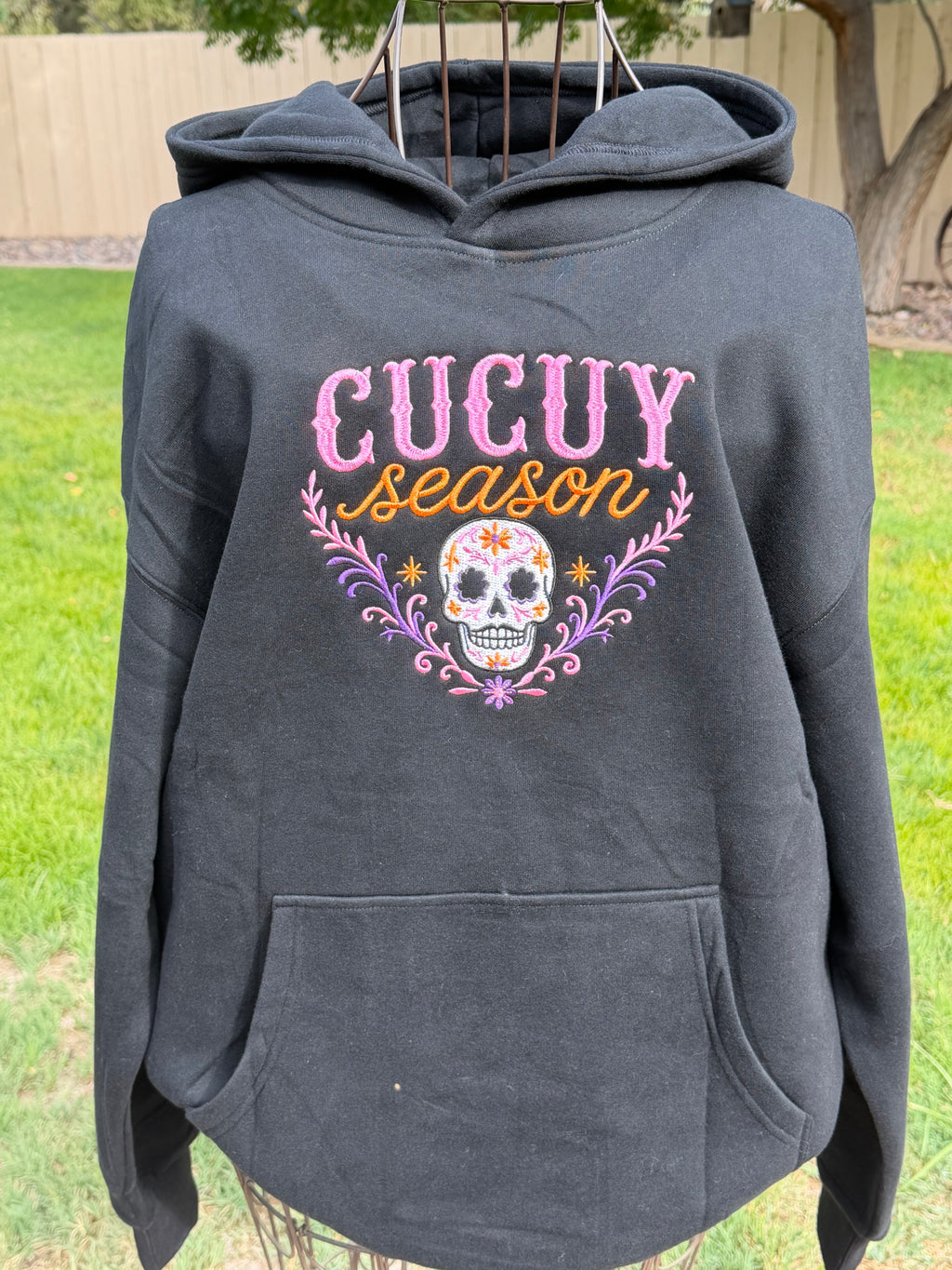 Black Cucuy Season embroidered hoodie featuring a colorful sugar skull design in pink, purple and orange.