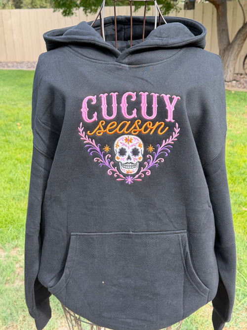 Black Cucuy Season embroidered hoodie featuring a colorful sugar skull design in pink, purple and orange.